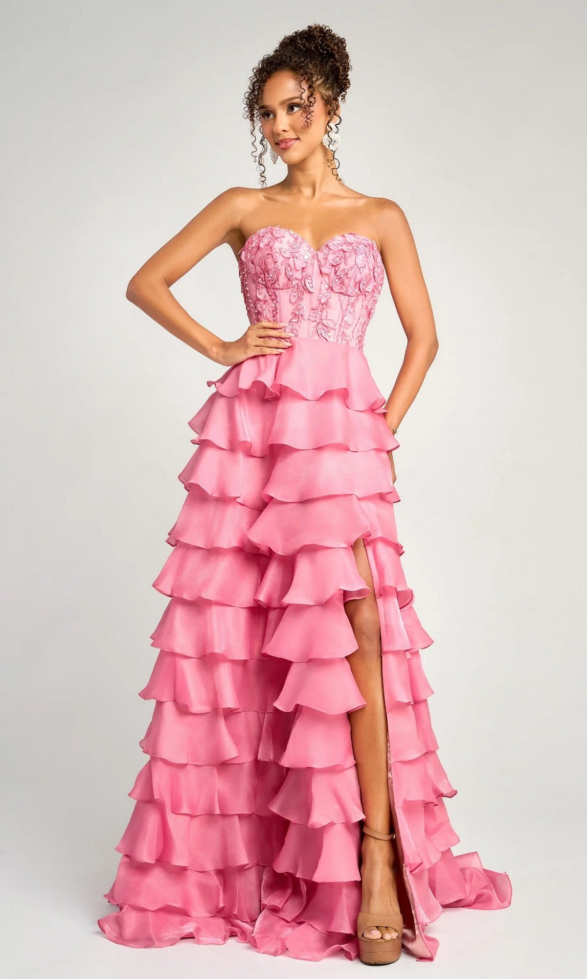 A woman stands against a plain light background wearing the Portia and Scarlett PS26048, a long formal pink strapless dress with a sweetheart neckline, tiered ruffles, floral-embroidered bodice, and thigh-high slit.